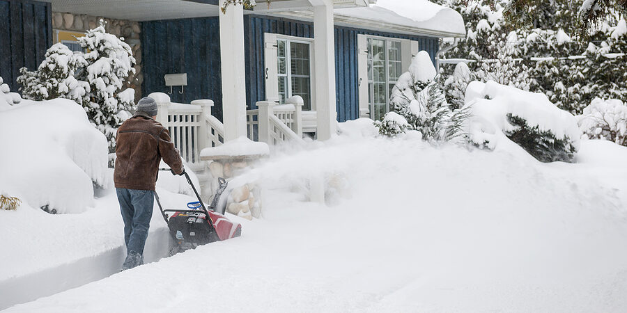 Man using snowblower to clear deep snow on driveway near residen